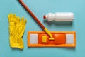Flat mop, floor cleaner and rubber gloves over blue background. Orange microfiber mop with handle, white bottle of liquid cleaner Royalty Free Stock Photo