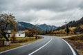 Flat new asphalt road in a mountain village, mountains in the fog, a white house and autumn trees Royalty Free Stock Photo