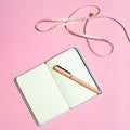 A flat notebook with a measuring tape on a pink background.