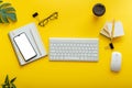 Flat office workspace on colorful yellow background. Office table desk with computer keyboard, glasses, smartphone mouse