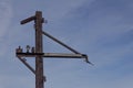 Flat steel poles with outriggers and light fixtures against blue sky, rusted metal patina