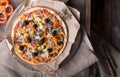 Flatbread pizza garnished with fresh arugula on wooden pizza board, top view. Dark stone background. Person picking slice of pizza Royalty Free Stock Photo