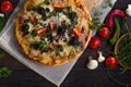 Flatbread pizza garnished with fresh arugula on wooden pizza board, top view. Dark stone background. Person picking slice of pizza Royalty Free Stock Photo