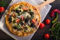 Flatbread pizza garnished with fresh arugula on wooden pizza board, top view. Dark stone background. Person picking slice of pizza