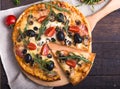 Flatbread pizza garnished with fresh arugula on wooden pizza board, top view. Dark stone background. Person picking slice of pizza