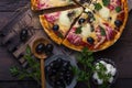 Flatbread pizza garnished with fresh arugula on wooden pizza board, top view. Dark stone background. Person picking slice of pizza