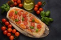 Flatbread pizza garnished with fresh cherry tomatoes, basil, cheese and olive oil on wooden pizza board.