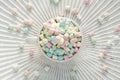 Flatlay of beige cup filled with pastel mini marshmallows on white wooden underground with rays and sprinkled marshmallows HR S