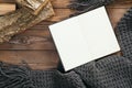 Flatlay book with empty page, grey knitted scarf, firewood on wooden background. Flat lay, top view, overhead. Cozy autumn home Royalty Free Stock Photo