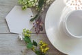 Flatlay close-up with an empty cup on a saucer with mockup an empty white card framed by branches of green leaves, white flowers