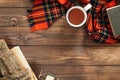 Flatlay composition with red scarf, cup of tea, firewood, book on wooden desk table. Hygge style, cozy autumn or winter holiday