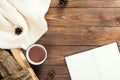 Flatlay composition with white knitted scarf, cup of tea, book with empty pages, firewood on wooden desk table. Hygge style, cozy Royalty Free Stock Photo