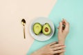 Flatlay with cut avocado on white plate and woman`s hands