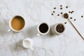 Flatlay of fresh cups of espresso and milk coffee, creamer, coffee beans and spoon on marble