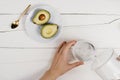 Flatlay with fresh ripe cut avocado halves and woman`s hand pouring clean water in a glass on wooden white table Royalty Free Stock Photo