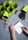 Flatlay with garden tools, green plant pots and hands is writting on notepad on concrete background