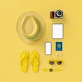 Flatlay with hat with sun glasses, t suitcase, slippers, hat, suntan cream, phone and camera on yellow minimal style background.