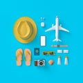 Flatlay with hat with sun glasses, toy plane, slippers, hat, suntan cream, phone and camera on blue minimal style background.