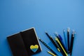 Flatlay horizontal composition black notebook pages, heart patch, black felt-tip pens with blank blue background