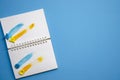 Flatlay horizontal composition open notebook with yellow and blue strokes of paint on white pages and blank blue background