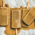 Flatlay of melting coffee latte popsicles on grey marble background