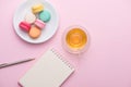 Flatlay of notebook, cake macaron and cup of tea on pink table. Royalty Free Stock Photo