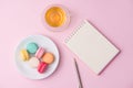 Flatlay of notebook, cake macaron and cup of tea on pink table.