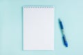 Flatlay notebook and pen on a table on a blue background.