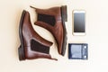 Flatlay of Pair of Classic Leather Chealsea Boots, Blue Leather Wallet, Cellphone Placed Near One Another On Beige Background