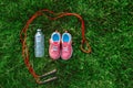 Flatlay with pair of pink girl sneakers shoes, jump rope and bottle of water in green grass