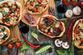 Flatlay of pizza party. Pizzas in abundance with raw vegetables, salami, mushrooms and red wine on dark oak chopping boards over Royalty Free Stock Photo