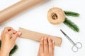 flatlay of process of wrapping Christmas gifts in craft wrapping paper, with decor of jute rope and fir branches