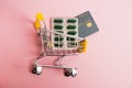 Flatlay, shopping cart, bank card and pills in a blister on a pink background