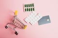 Flatlay, shopping cart, bank card and pills in a blister on a pink background