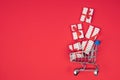 Flatlay shopping cart full of flying gifts on a red background with copy space. Holidays, discounts and christmas concept