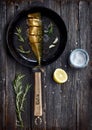 Flatlay of slice fried fish on a fry pan decorated with rosemary, garlic, lemon and salt on wooden surface