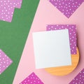 Flatlay square note sheets,round wooden base,pink green diagonal paper backdrop,lilac paper with white polka,copy space.