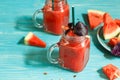 Two glass mugs with watermelon smoothie decorated with red Basil leaves. Watermelon slices on a blue wooden background. and