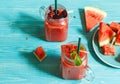 Two glass mugs with watermelon smoothie decorated with red Basil leaves. Watermelon slices on a blue wooden background