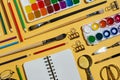 Flatlay of watercolors, brushes, notebooks and other stationery and art supplies on yellow