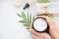 Flatlay. Woman putting nutritious cream on her hands on white background among jar of cosmetic cream, leaf palm branch