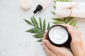 Flatlay. Woman putting nutritious cream on her hands on white background among jar of cosmetic cream, leaf palm branch