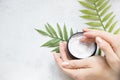 Flatlay. Woman putting nutritious cream on her hands on white background among jar of cosmetic cream, leaf palm branch