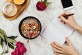 Flatlay of woman`s hands with notebook and smartphone, vegan smoothie bowl with chia pudding on marble