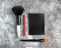 Composition of cosmetic makeup brushes in black, red eyeliner and black phlox on a gray cement background. Flatley