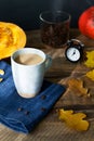 Flavored pumpkin coffee with spices in a ceramic cup on a blue napkin with orange pumpkins and dry leaves in the background.]