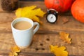 Flavored pumpkin coffee with spices in a ceramic cup on a wooden table with orange pumpkins and dry leaves in the background