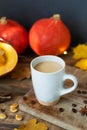 Flavored pumpkin coffee with spices in ceramic cups on a wooden table with orange pumpkins and dry leaves in the background