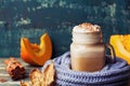 Flavored pumpkin spiced latte or coffee in cup decorated knitted scarf on teal vintage background. Autumn, fall, winter hot drink.