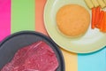 Flavored raw meat steak for cook on non stick pan with round shape or berger bread and sliced carrots with corn in plate on Royalty Free Stock Photo